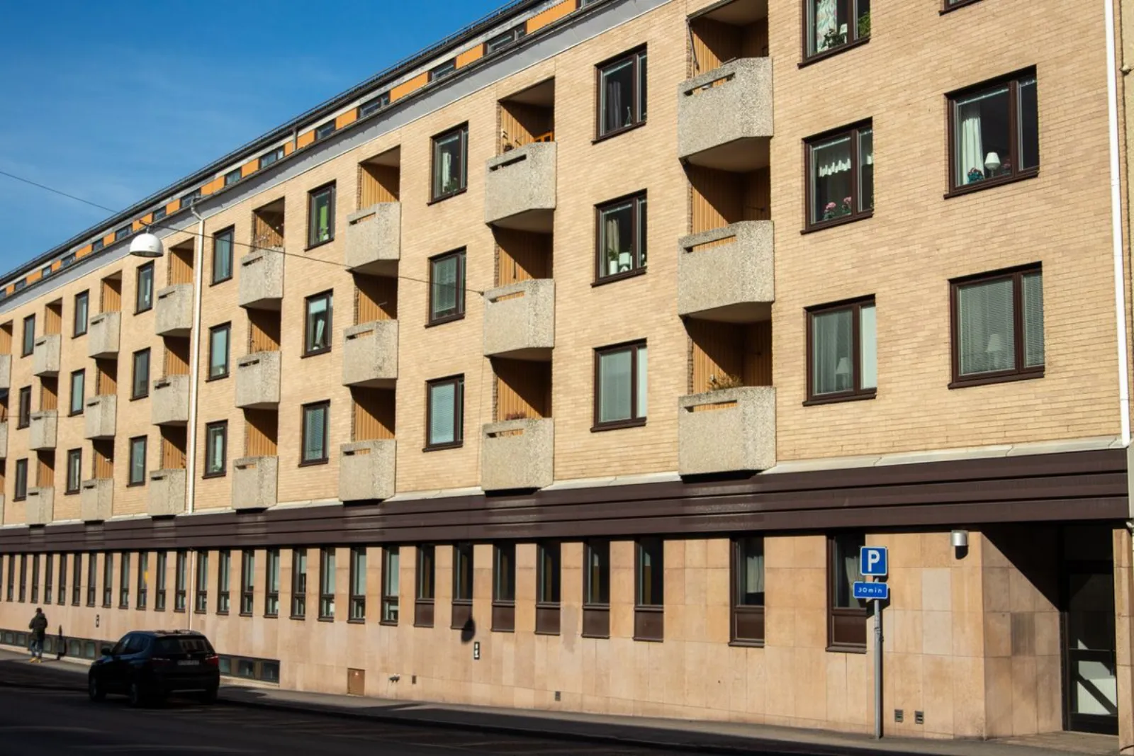 Långt bostadshus i gult tegel längs en gata med parkeringsskylt