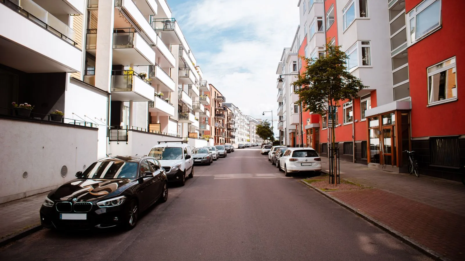 Nybyggda flerfamiljshus längs en bostadsgata med parkerade bilar på båda sidor